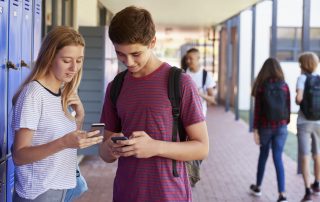 Two friends talking and using phones in school corridor