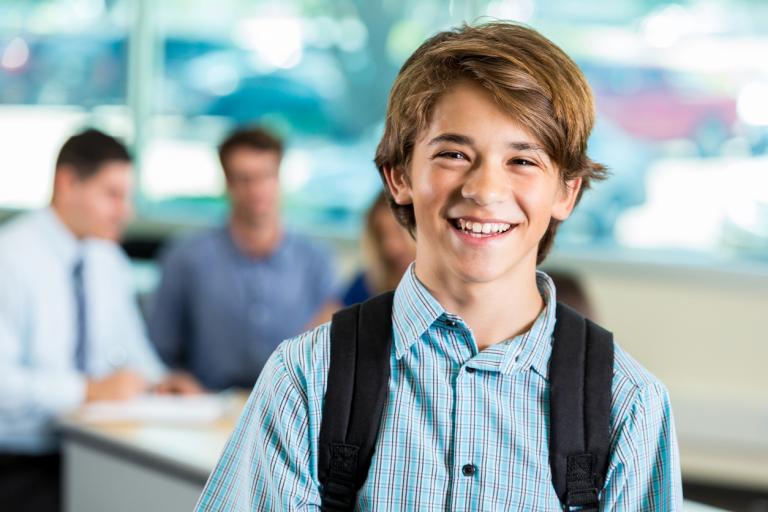 Teenage boy is wearing a backpack and standing in classroom in secondary school