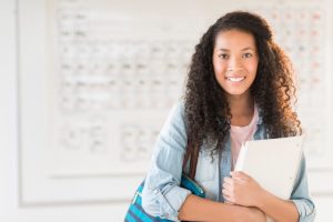 Portrait of beautiful teenage student feeling stress free with shoulder bag and books standing in chemistry class