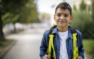 Smiling teenage boy with school bag in front of school. Difficulties international students face concept