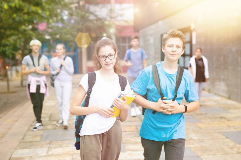 Group of high schoolers with backpacks and workbooks walking inside a campus.