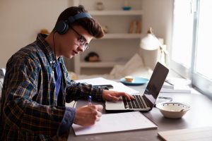 Teenage boy wearing headphones working at desk to finish the semester strong