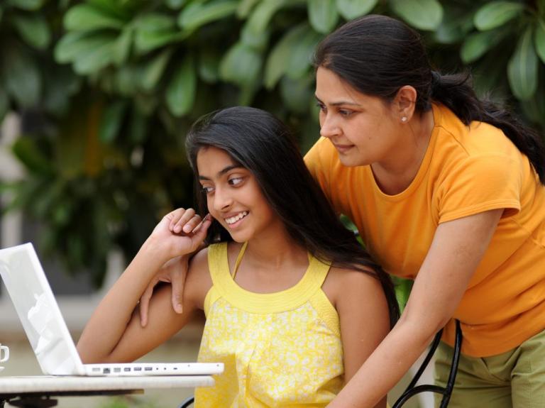 Mother and daughter are looking at a laptop outdoors. International students and private school research.