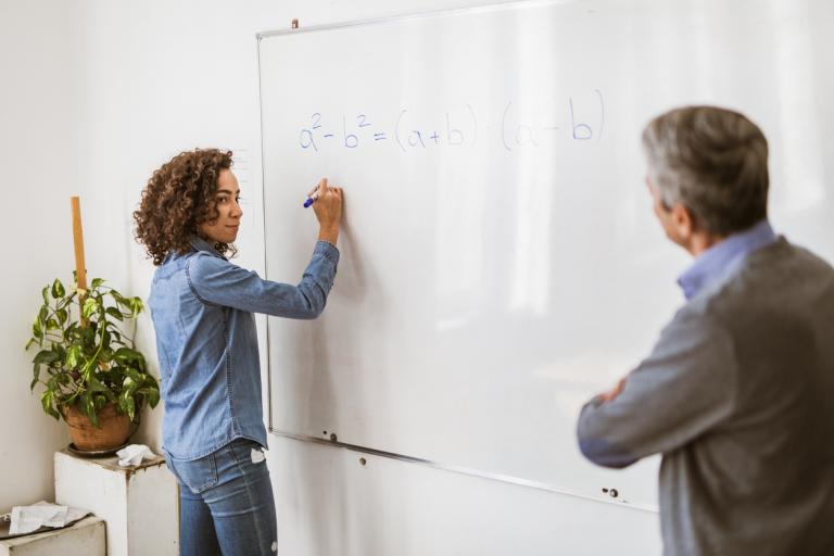 Student writing a formula on whiteboard while her teacher is using differentiated instruction to teach