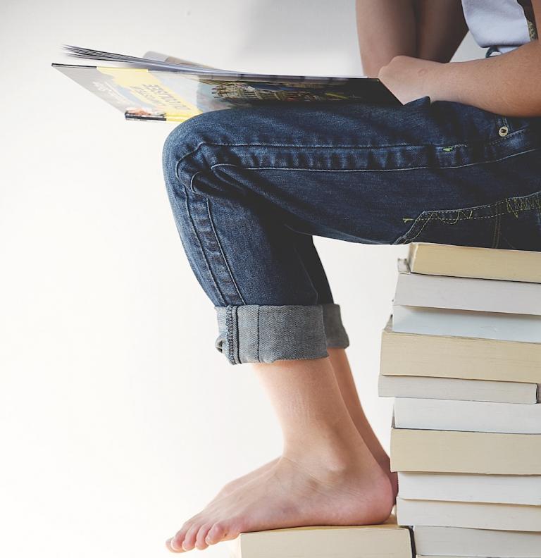 Gifted and talented student sits on a stack of books reading