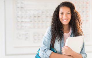 Portrait of beautiful teenage student feeling stress free with shoulder bag and books standing in chemistry class