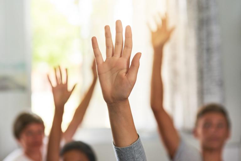 Shot of unidentifiable schoolchildren raising their hands to answer a question in class