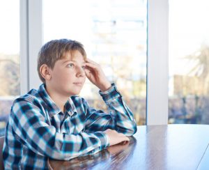 12 years old boy sitting at the wooden desk, composition against the window thinking about private schools