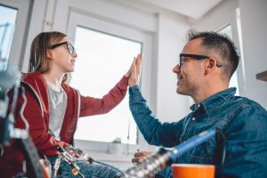 Father and daughter talking about alternative school while working on electronics components at home office and cheering after successful testing