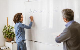 Student writing a formula on whiteboard while her teacher is using differentiated instruction to teach