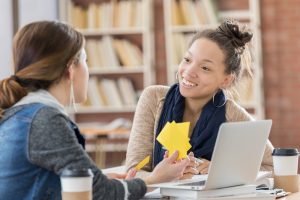 Diverse female students use notecards to study for an exam. They are also using a laptop computer. Customized instruction concept