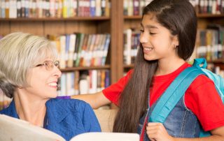 Teacher uses customized curriculum to read a book to a female elementary age student in school library.