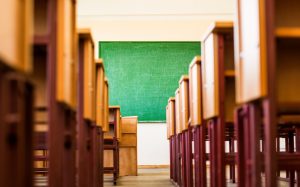 An image of a university or school classroom taken almost from the floor, depicting a path between desks guiding to the old scratched green blackboard hanging on a wall.