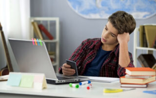 Young student browsing his cellphone while doing homework to suggest time blindness.