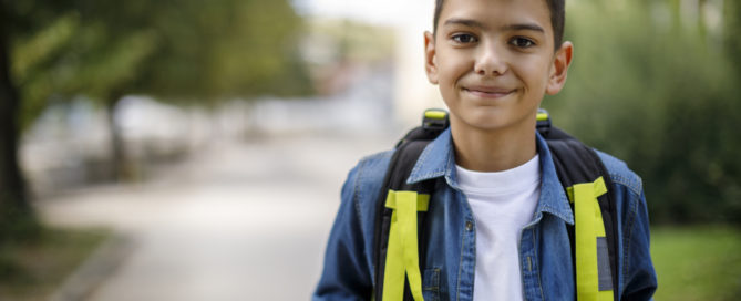 Smiling teenage boy with school bag in front of school. Difficulties international students face concept
