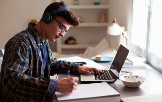Teenage boy wearing headphones working at desk to finish the semester strong