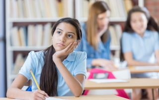 Cute Hispanic middle school girl looks away while daydreaming in class. Struggle with writing concept