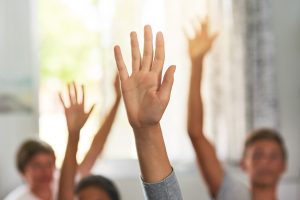 Shot of unidentifiable schoolchildren raising their hands to answer a question in class