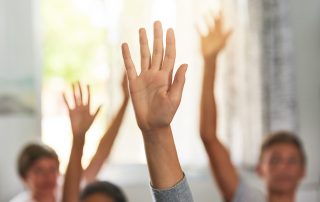 Shot of unidentifiable schoolchildren raising their hands to answer a question in class