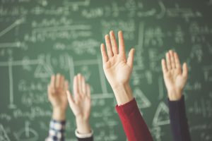 Students raised up hands green chalk board in classroom. Questions in Class