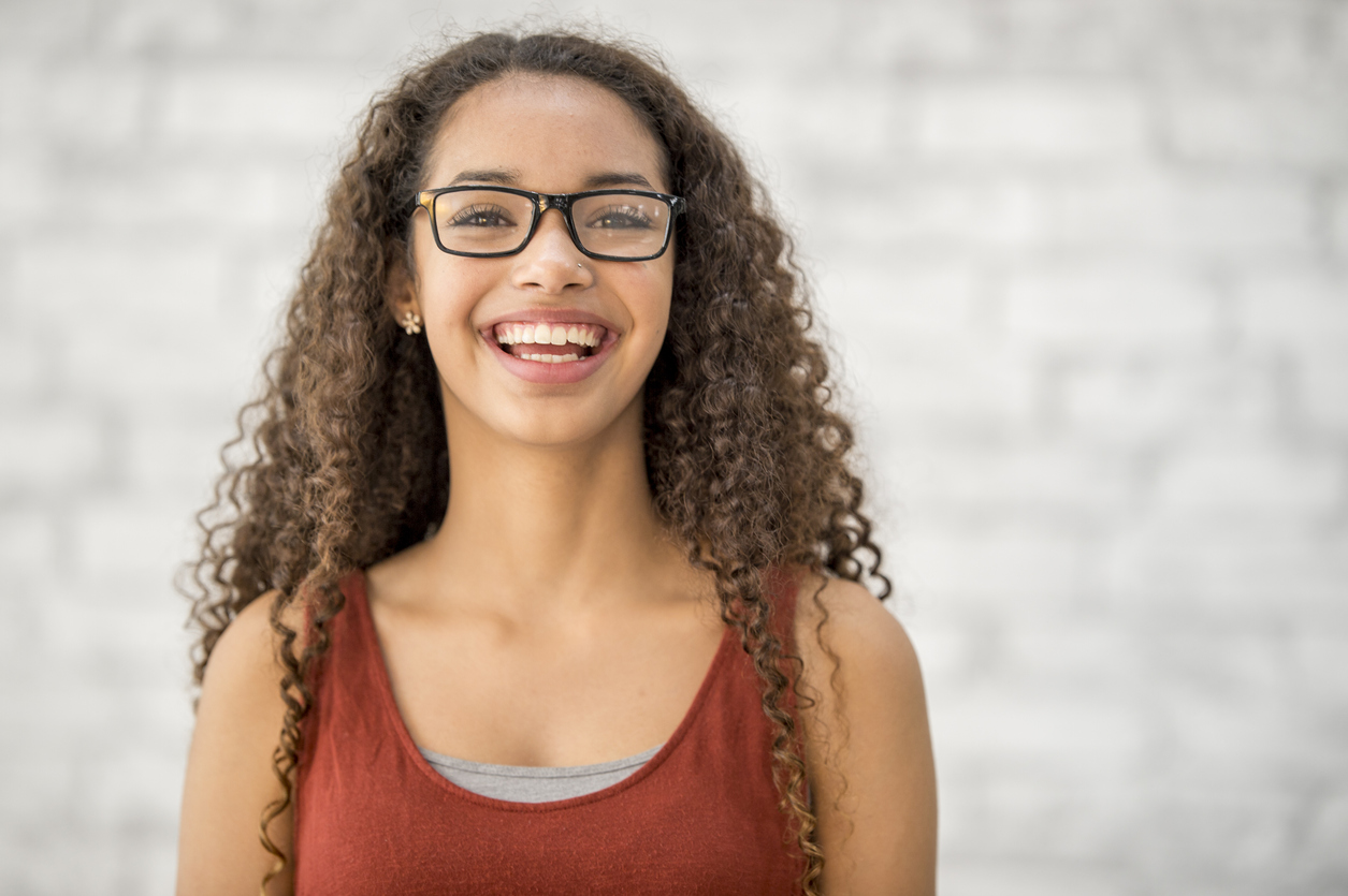 A teenage girl with long curly hair in a gifted and talented program at school. She is wearing glasses and a tank top. She is smiling at the camera.