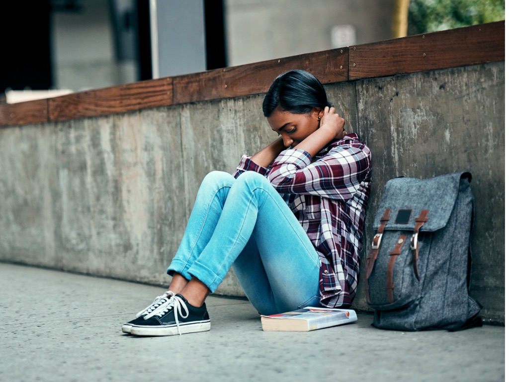 Student anxiety concept, teen girl hunched over against a wall outside