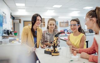 Point of view angle of teenage girls studying robotic arm in a private school.