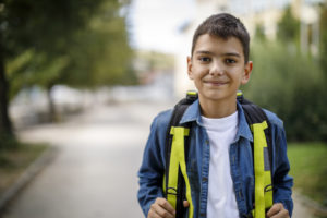 Smiling teenage boy with school bag in front of school. Difficulties international students face concept