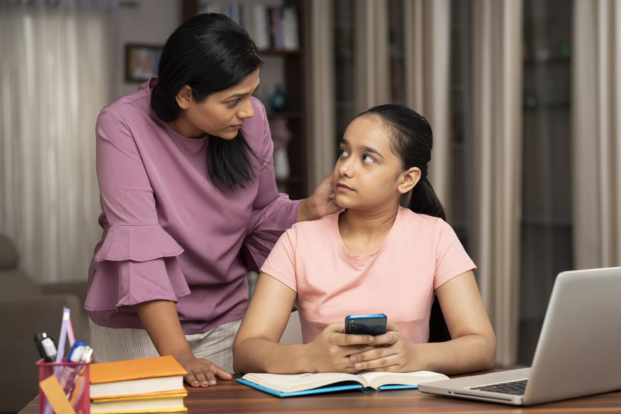 The mother is talking to her teenage daughter while the daughter is studying in her study area.