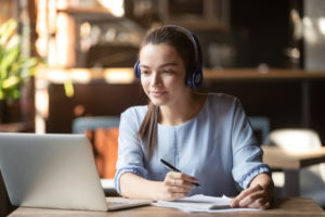 female-student-wearing-headphones-while-writing-notes-online-education-concept