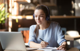 female-student-wearing-headphones-while-writing-notes-online-education-concept