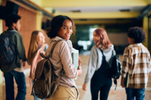 High school student walking through the hallway with her friends, considering whether to switch schools.