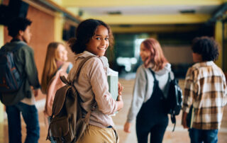 High school student walking through the hallway with her friends, considering whether to switch schools.